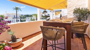 Un espace de restauration en plein air avec un auvent jaune, des chaises en osier et une table dressée pour deux personnes.