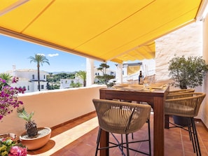 An outdoor dining area with a yellow canopy, wicker chairs, and a table set for two. - 3 Bedroom Townhouse Aldea Blanca (Marbella)