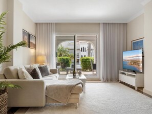 A modern living room with a sofa, a television, and a view of a courtyard.