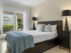 A hotel room with a large bed, two bedside tables with lamps, a view of buildings outside, and a balcony.