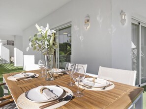An outdoor dining area with a wooden table set for four, surrounded by white chairs, and a vase with white flowers. - Terrazas DE Banus 4 12 (Marbella)