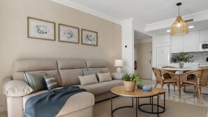 Uma sala de estar com sofá, mesa de centro redonda e um espaço de jantar com cadeiras de vime.