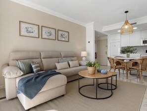 Ein Wohnzimmer mit einer Couch, einem runden Couchtisch und einem Essbereich mit Korbstühlen.