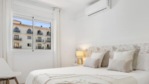 Et hotelværelse med seng, stol, et natbord med lampe og udsigt til bygninger gennem vinduet.
