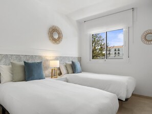 Ein Schlafzimmer mit zwei Betten, einem Fenster mit Blick auf Gebäude und einem wandmontierten Spiegel.