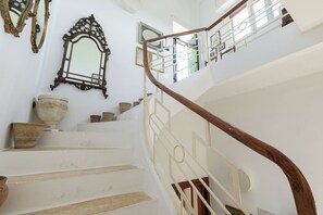 Un escalier avec des marches blanches et une rampe en bois, menant à un palier agrémenté d’une balustrade et de tableaux encadrés.