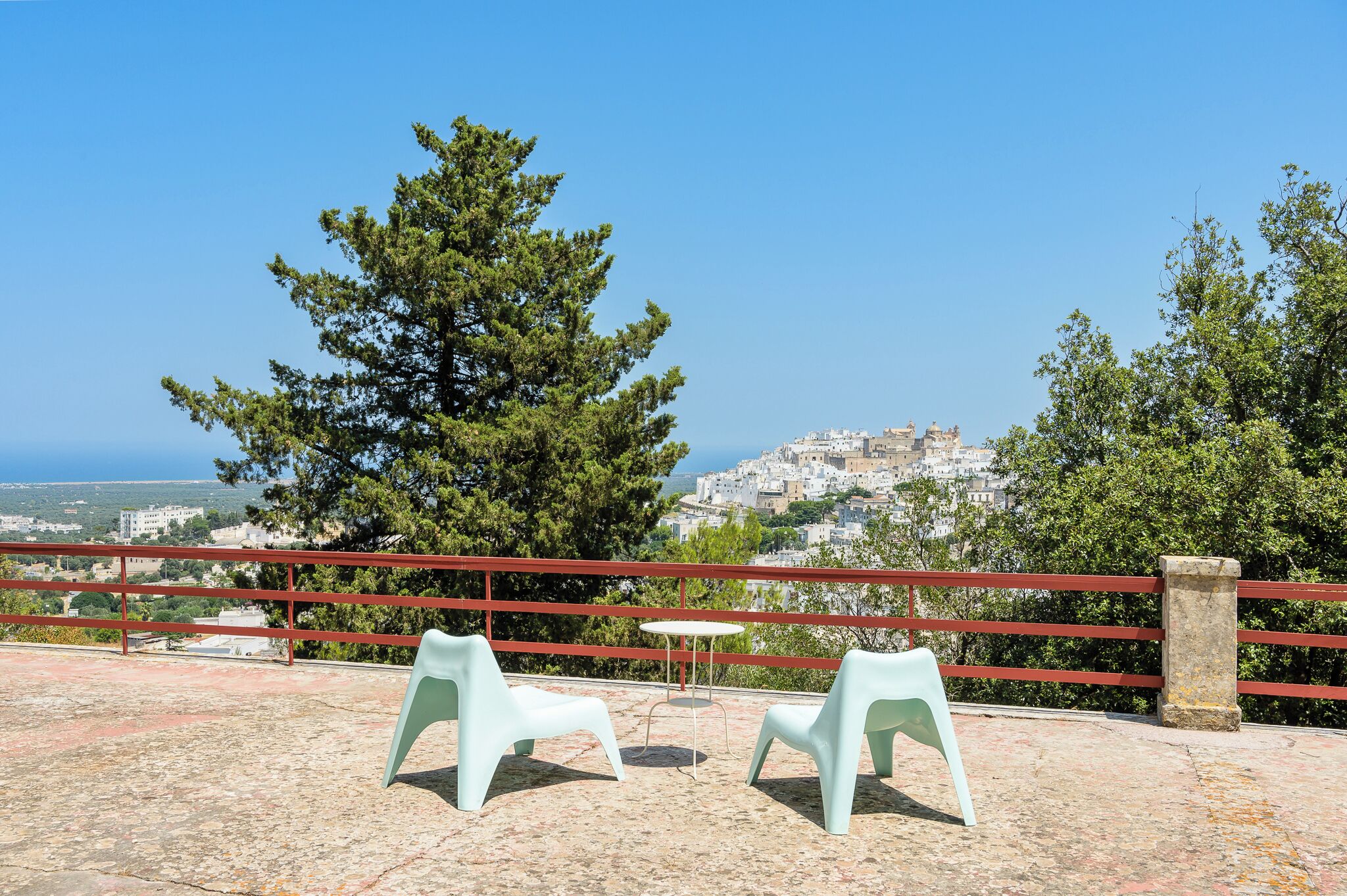 A terrace with two plastic chairs and a small table, overlooking a coastal town with a prominent church.