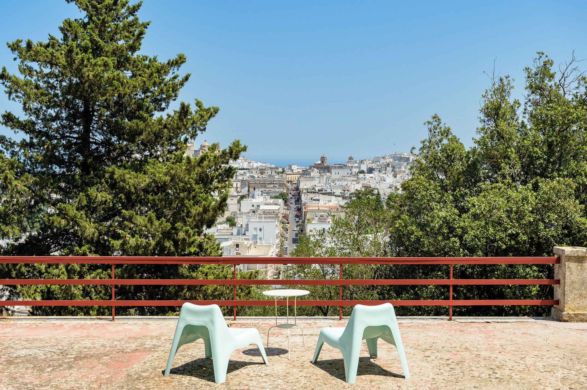 A terrace with two chairs and a table, overlooking a densely packed cityscape with buildings and a clear sky.