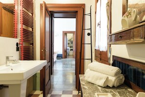 Un baño con lavamanos, espejo, toallero y vista a la habitación contigua.