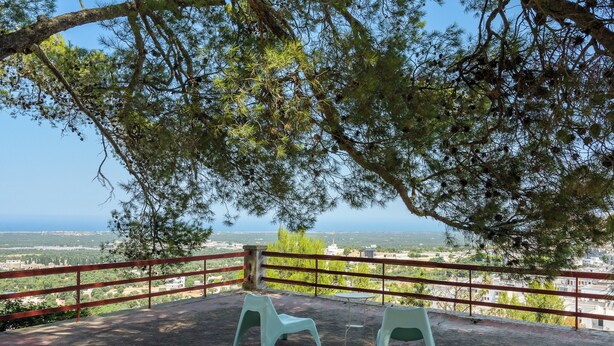 Terraço com duas cadeiras e uma mesa, com vista para a paisagem costeira.