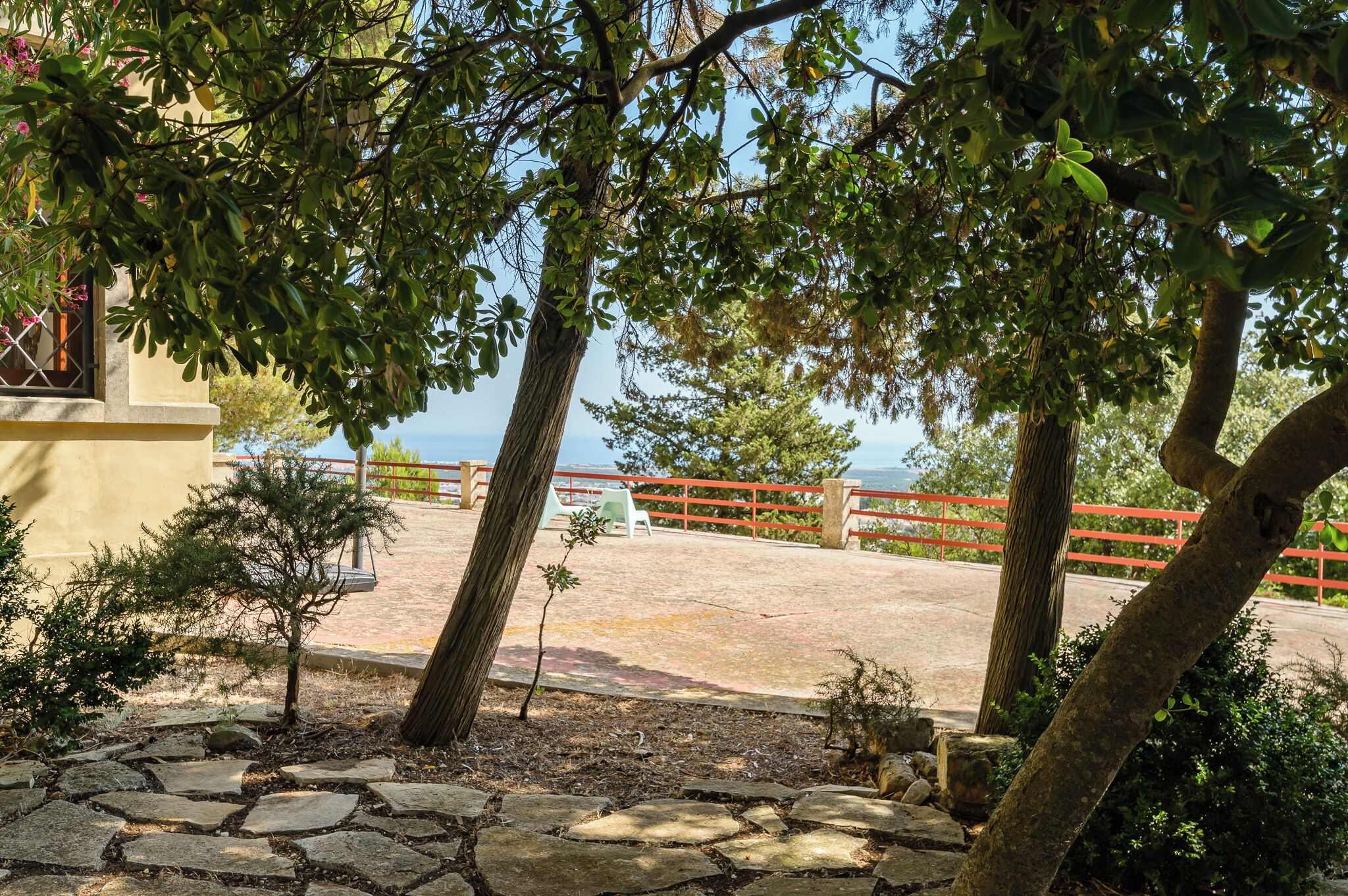 A paved area with stone tiles, a red railing, and trees.