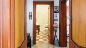 Um corredor com portas de madeira, chão xadrez e uma pequena mesa com um cesto.