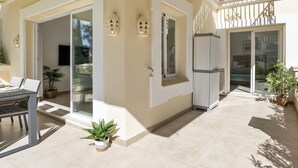 A modern outdoor living area with a dining table, potted plants, and a sliding glass door leading to a bedroom. - Andalucia del Mar 10 06 (Marbella)
