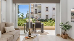 A modern living room with a sofa, a coffee table with a bottle and glasses, and a view of a balcony with outdoor furniture and a building in the background. - Andalucia del Mar 10 06 (Marbella)