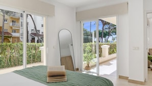 A bedroom with a bed, a large mirror, and a view of a balcony with plants and a building. - Andalucia del Mar 10 06 (Marbella)