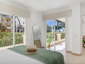 Ein Schlafzimmer mit einem Bett, einem großen Spiegel und Blick auf einen Balkon mit Pflanzen und einem Gebäude.