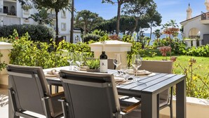 An outdoor dining area with a table set for two, surrounded by lush greenery and overlooking a body of water. - Andalucia del Mar 10 06 (Marbella)