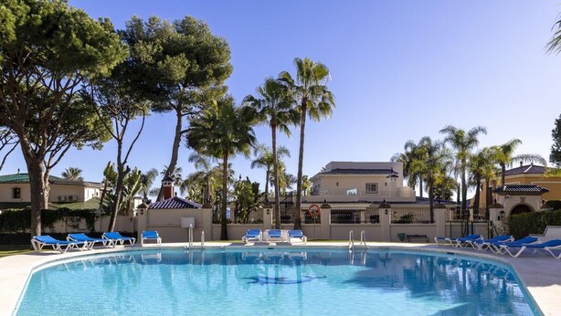 A clear swimming pool with blue tiles, surrounded by lounge chairs and palm trees. - Andalucia del Mar 10 06 (Marbella)