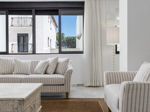 Ein modernes Wohnzimmer mit einem gestreiften Sofa, einem kleinen Tisch und Blick auf ein Gebäude durch große Fenster.