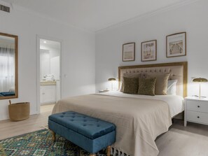 Ein Schlafzimmer mit einem großen Bett, Nachttischen, einer Bank und gerahmten Bildern an der Wand.