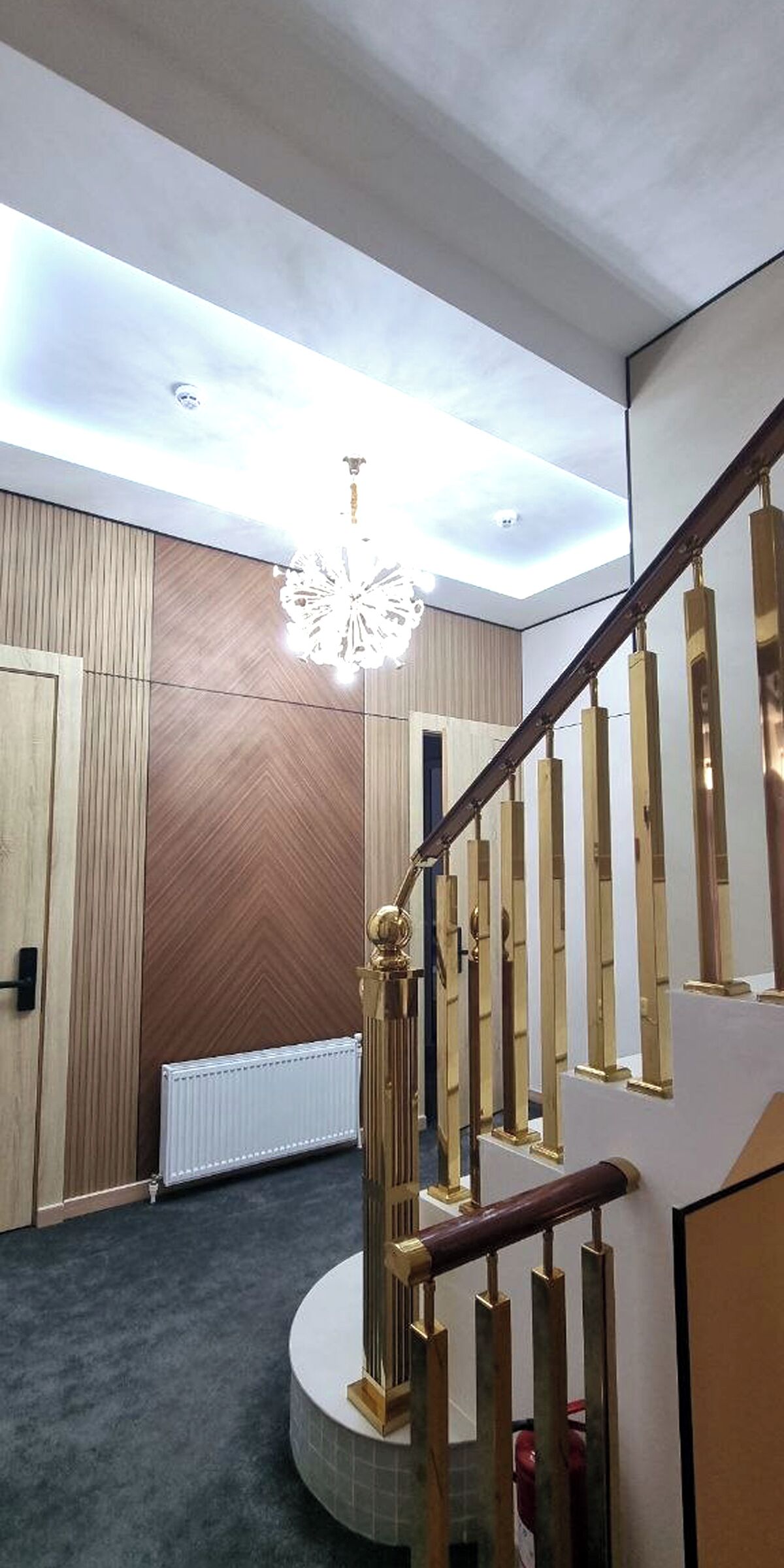 A modern interior with a wooden wall, a white radiator, and a staircase with a golden handrail.