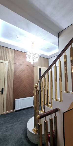 A modern interior with a wooden wall, a white radiator, and a staircase with a golden handrail. - Maftun hotel (Samarkand)