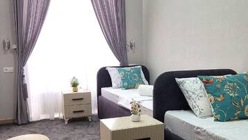 A bedroom with a bed, a bedside table, a small stool, and a window with curtains.