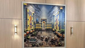 Una habitación con un gran mural que muestra un edificio histórico, dos sillones tapizados, una pequeña mesa redonda con una lámpara y un control remoto.