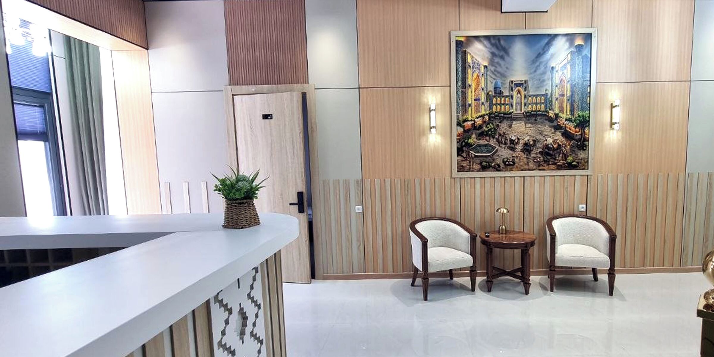 Uma área de recepção com balcão, dois poltronas, uma mesinha e um quadro na parede.