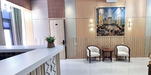 A reception area with a reception desk, two armchairs, a small table, and a painting on the wall. - Maftun hotel (Samarkand)