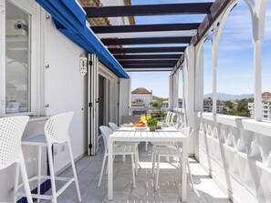Ein Balkon mit einem weißen Tisch und Stühlen, einer blauen Markise und Blick auf Gebäude im Hintergrund.