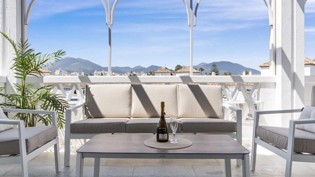 A terrace with a sofa, a table, and a bottle of wine, overlooking a mountainous landscape. - 01 bdr Casa Sevilla 604 (Marbella)
