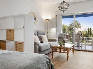 A modern bedroom with a bed, a sofa, a small table, and a balcony with outdoor furniture. - Estudio Medina Garden 232 (Marbella)