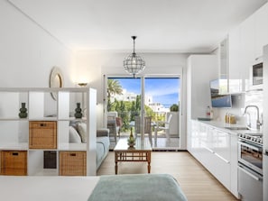A modern kitchen with white cabinets, a built-in oven, and a dining area with a table and chairs. - Estudio Medina Garden 232 (Marbella)