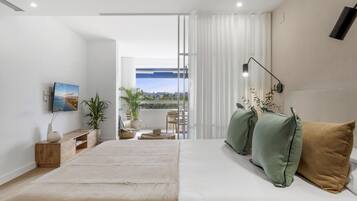 Un dormitorio moderno con una cama grande, un televisor montado en la pared y vistas al exterior a través de una puerta corredera.