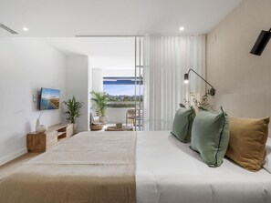 Ein modernes Schlafzimmer mit einem großen Bett, einem an der Wand montierten Fernseher und Blick ins Freie durch eine Schiebetür.