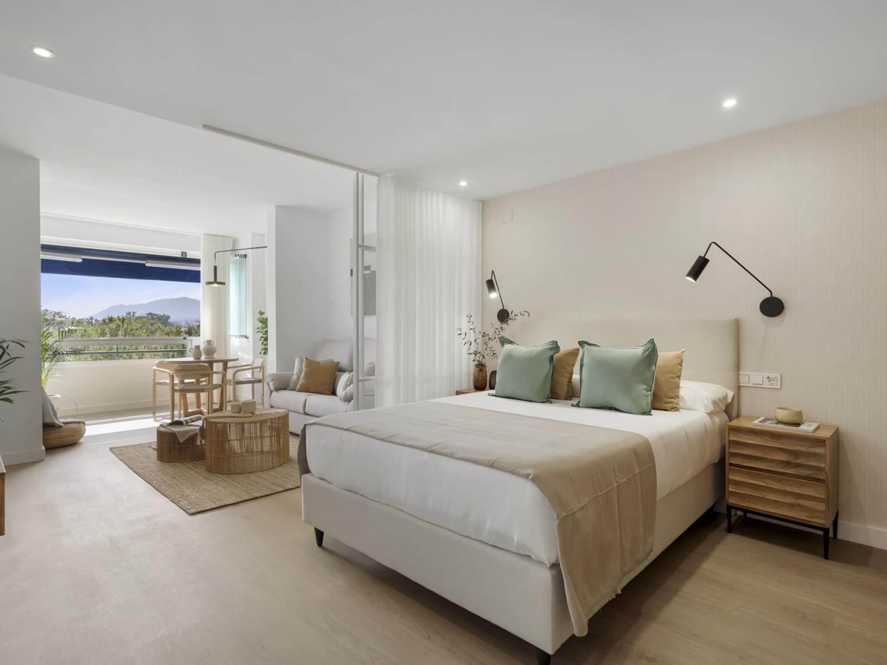 Un dormitorio moderno con una cama grande, mesitas de noche, un escritorio y vistas al exterior.