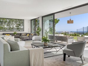 Ein modernes Wohnzimmer mit einer großen Glaswand, einer Sofagarnitur, einem Couchtisch und Blick ins Freie.