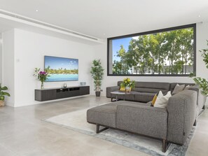 Ein modernes Wohnzimmer mit grauem Sofa, Flachbildfernseher und großem Fenster mit Blick auf Bäume.
