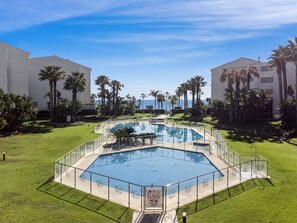 Ein Poolbereich mit geometrischem Design, umgeben von Palmen und blauem Himmel.