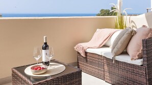 Ein Balkon mit einer Rattan-Couch, einem Tisch mit einer Weinflasche, Gläsern und einer Schale Erdbeeren.