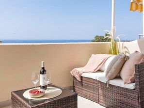 A balcony with a wicker sofa, a table with a bottle of wine, glasses, and a bowl of strawberries. - Andalucia del Mar 14 61 (Marbella)