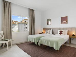 A hotel room with two beds, a chair, a window with curtains, and artwork on the wall. - Andalucia del Mar 14 61 (Marbella)