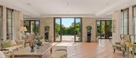 Un salón amplio con una mesa grande, sofás y vistas a un jardín a través de puertas de vidrio.