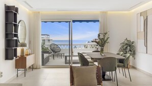 Ein modernes Wohnzimmer mit Balkon und Meerblick, ausgestattet mit einem Esstisch und Stühlen sowie einem großen Spiegel an der Wand.