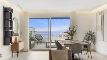 Una sala de estar moderna con balcón con vista al mar, amoblada con una mesa de comedor y sillas, y un espejo grande en la pared.