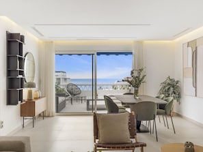 Ein modernes Wohnzimmer mit Balkon und Meerblick, ausgestattet mit einem Esstisch und Stühlen sowie einem großen Spiegel an der Wand.