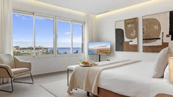 Un dormitorio moderno con una cama grande, una silla, un televisor y vistas al mar.