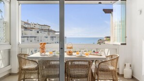 Ein Balkon mit Korbstühlen, einem Frühstückstisch und Blick auf das Meer und die Gebäude.