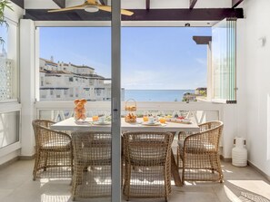 Ein Balkon mit Korbstühlen, einem Frühstückstisch und Blick auf das Meer und die Gebäude.